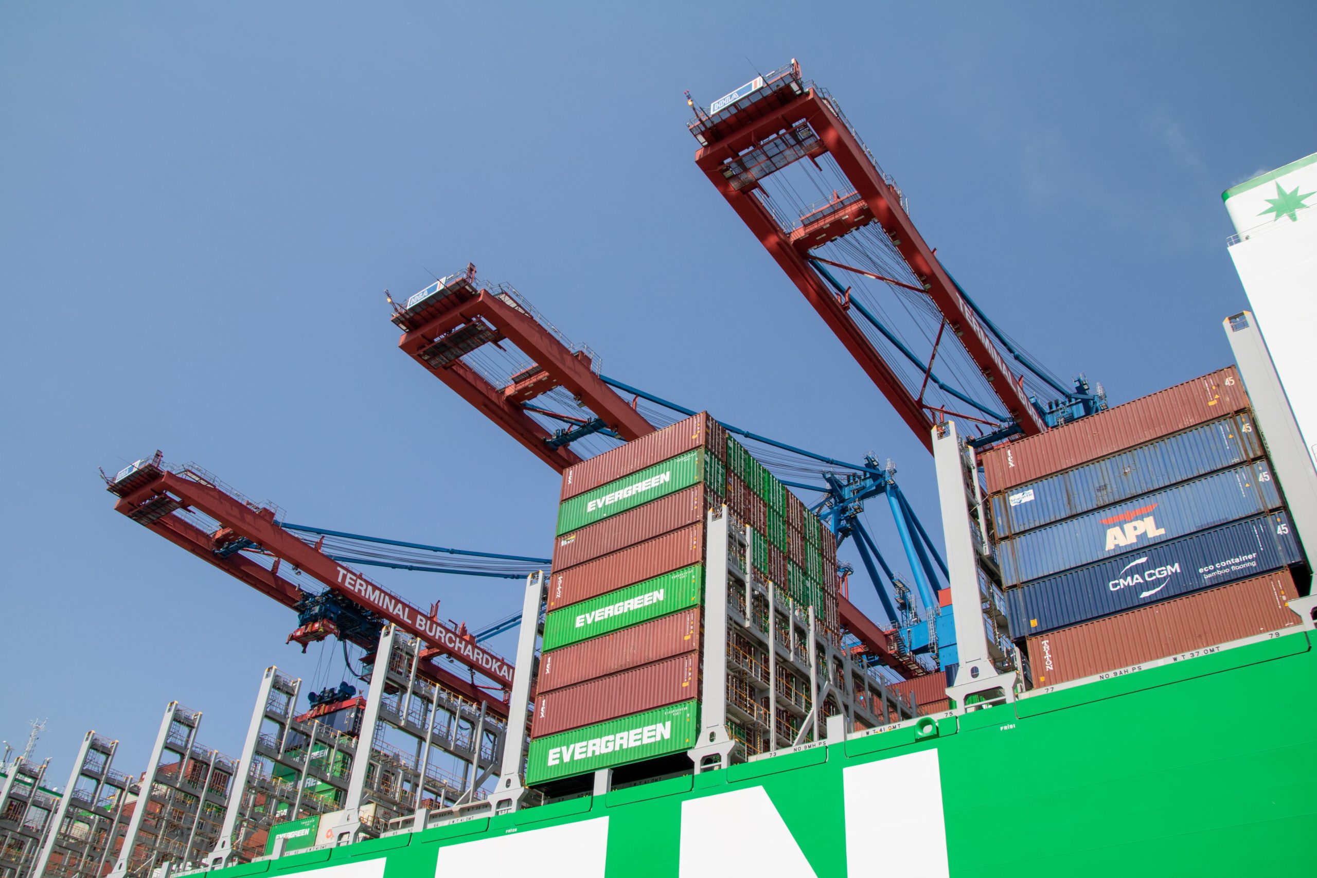 Low-angle view of cargo cranes and shipping containers at Hamburg port under clear sky.